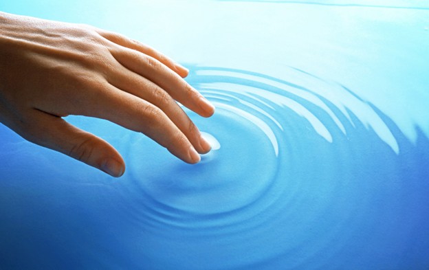 a light-skinned hand touches blue water causing rings